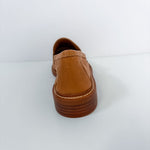 A single tan leather slip-on shoe shown from the back, featuring a thick brown platform sole with visible stitching, set against a plain white background.