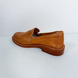 A single tan leather penny loafer with a stacked brown heel, photographed from a side angle against a plain white studio background.