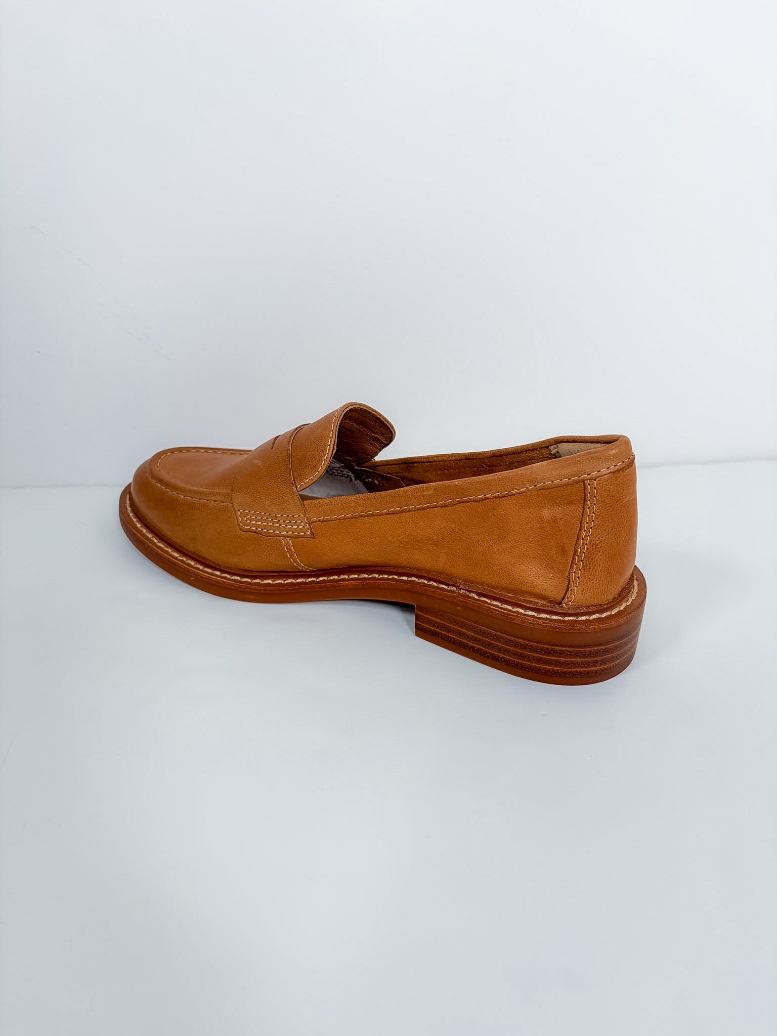 A single tan leather penny loafer with a stacked brown heel, photographed from a side angle against a plain white studio background.