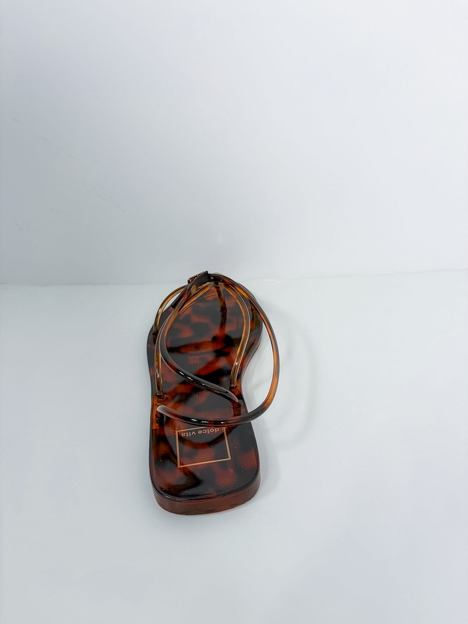 A single flat thong sandal in a glossy tortoiseshell pattern, featuring a small gold-tone metal brand plaque on the toe bed. The brand name 'SARABINO' is clearly visible on the plaque.