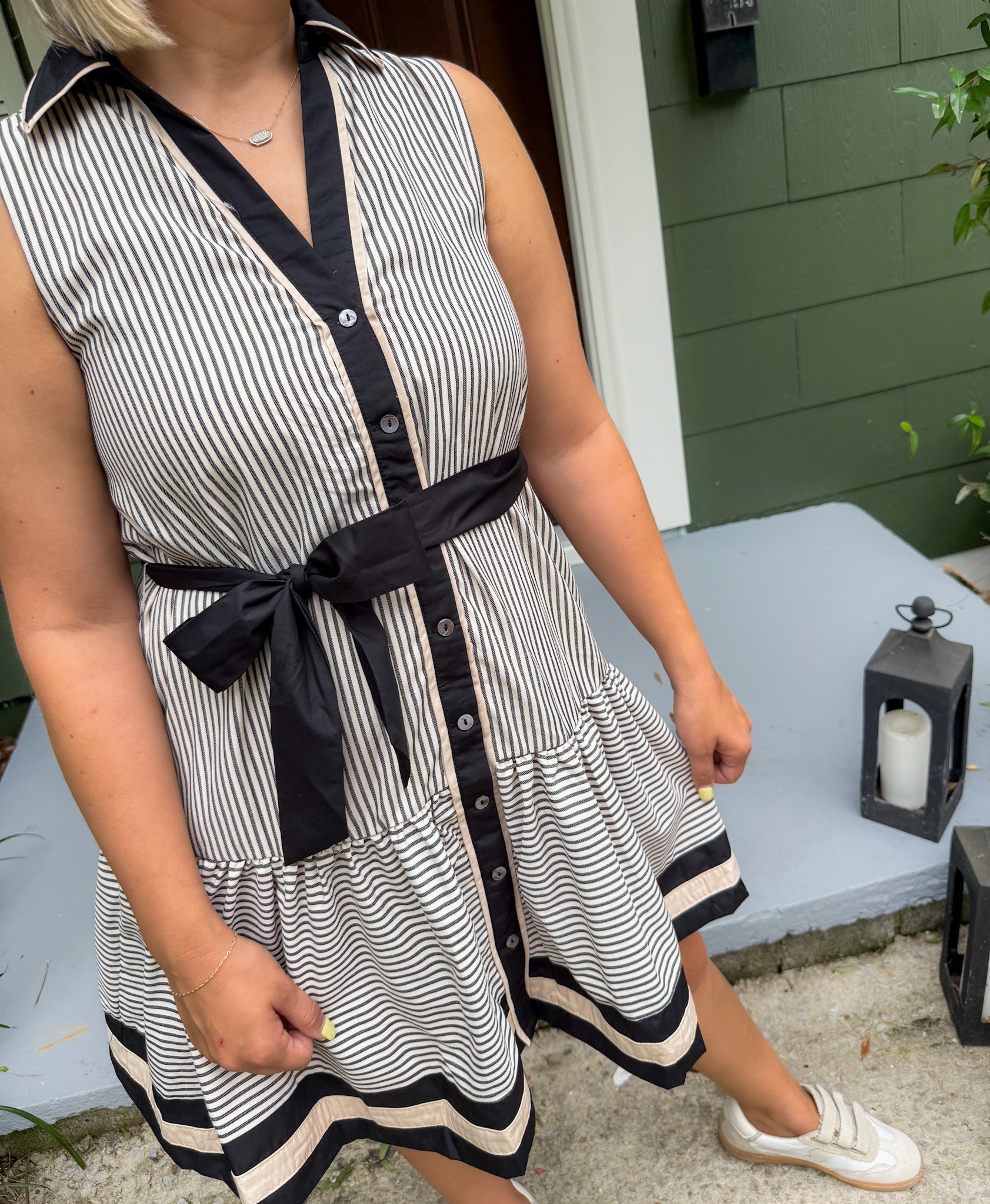 Woman wearing a black and white striped dress with a belt, standing outdoors.
