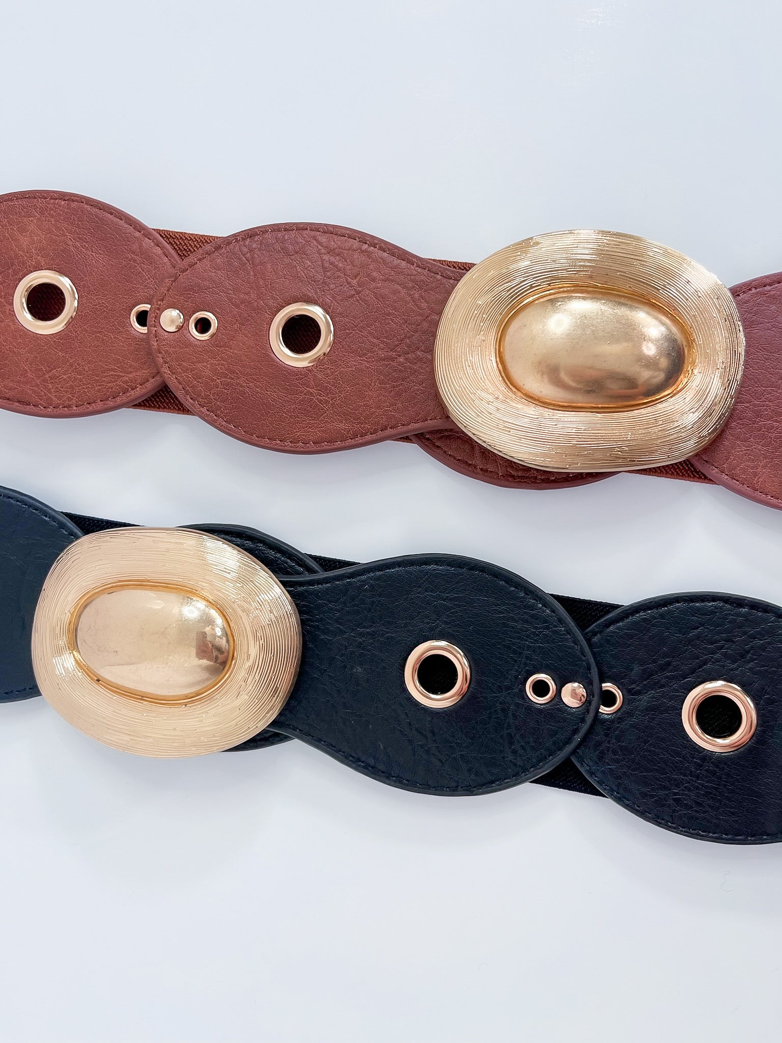 Two leather belts with gold oval buckles on a light gray background
