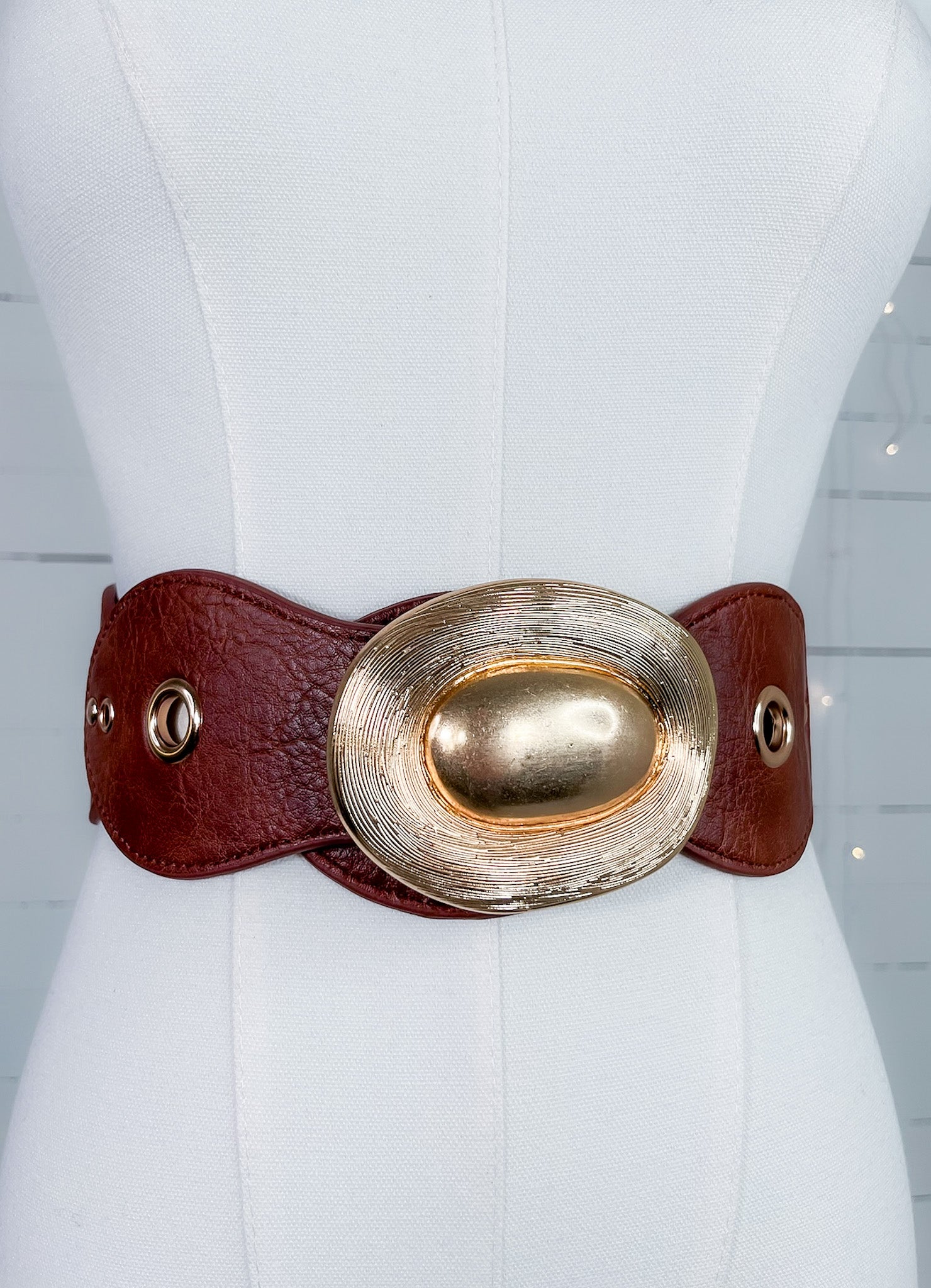 Mannequin wearing a wide brown leather belt with a large gold buckle.