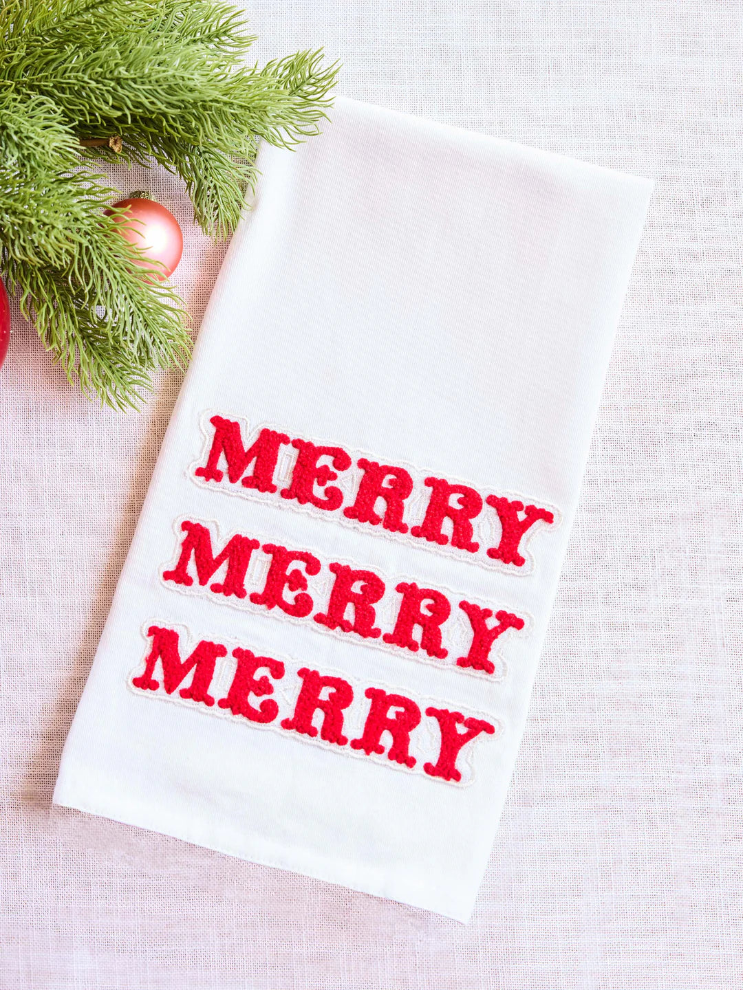 White towel with red 'MERRY' text on a light background with Christmas decorations.