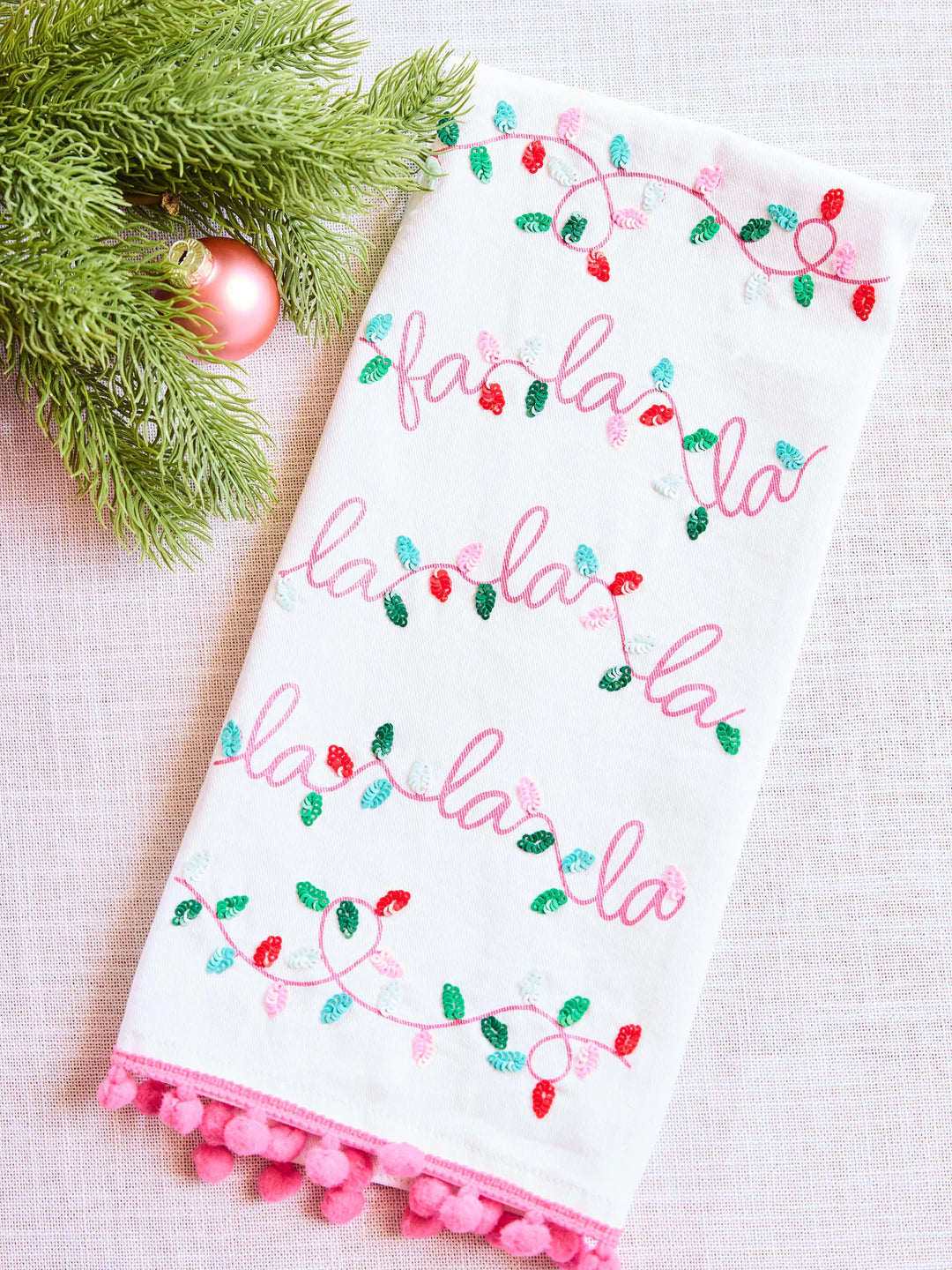 Decorative towel with 'fa la la' text and Christmas lights design on a white background.