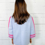 Person wearing a light blue jacket with pink accents against a white wooden panel background