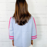 Person wearing a light blue jacket with pink accents against a white wooden panel background