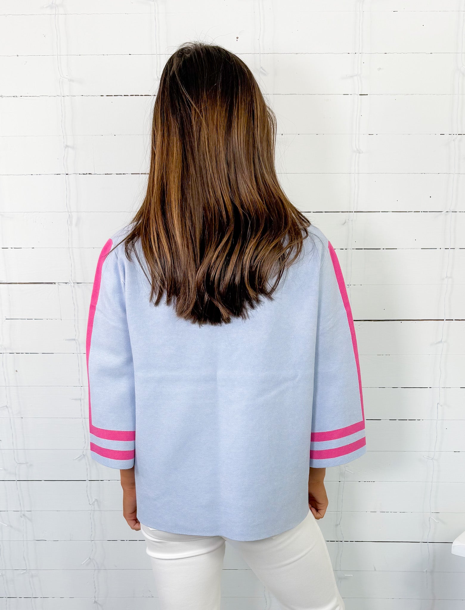 Person wearing a light blue jacket with pink accents against a white wooden panel background