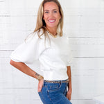 Woman wearing a white blouse and blue jeans against a white wooden panel background