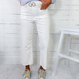 Person wearing a light blue sweater, white high-waisted jeans, and beige sneakers against a white wooden panel background.