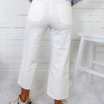 Person wearing white pants and a light blue sweater against a white wooden panel background