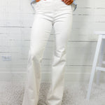 Person wearing light blue sweater and white flared jeans against a white wooden panel background