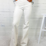 Person wearing light blue sweater and white flared jeans against a white wooden panel background