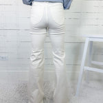 Person wearing white jeans and a blue striped shirt against a white wooden panel background