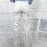 Person wearing white jeans and a blue striped shirt against a white wooden panel background