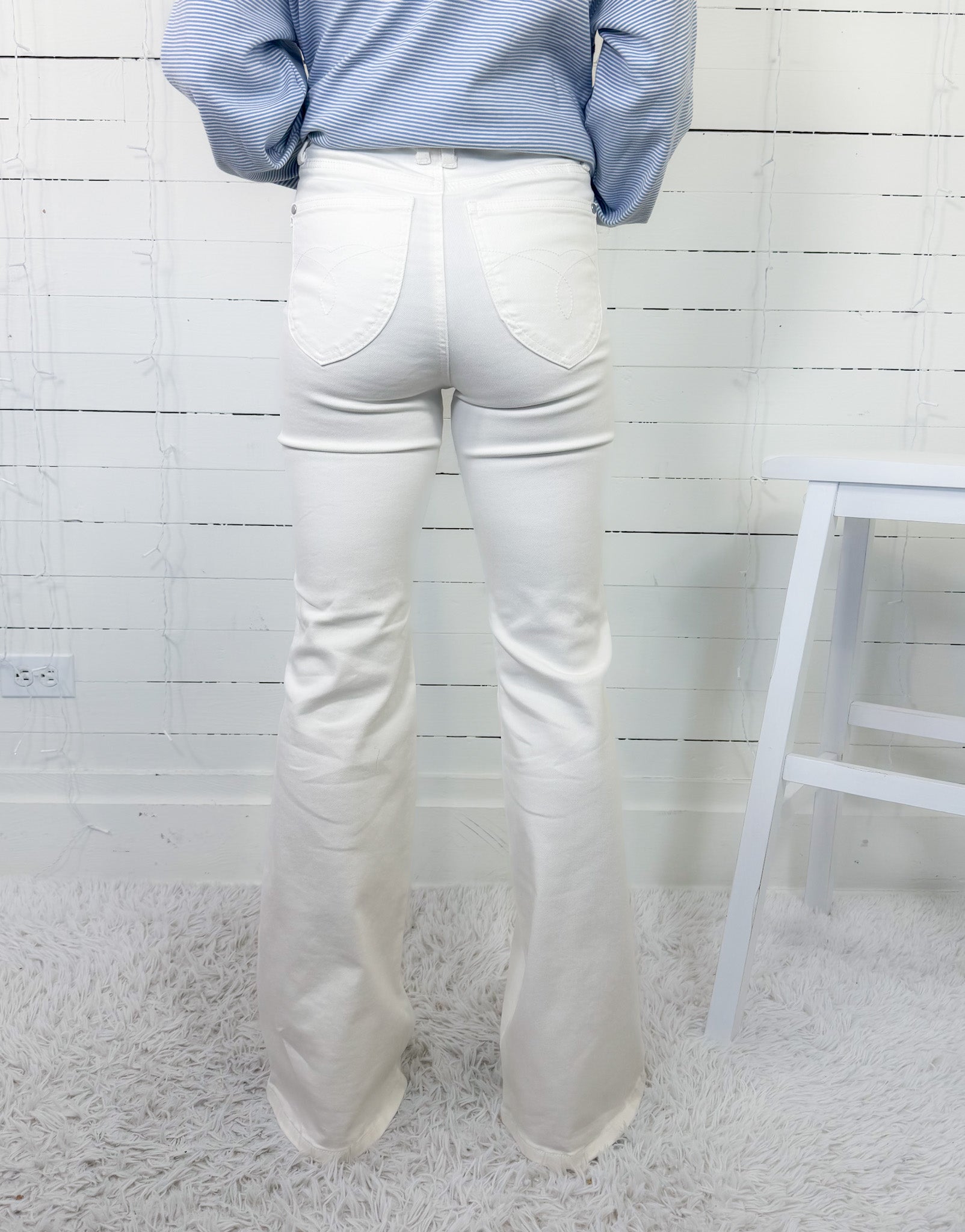 Person wearing white jeans and a blue striped shirt against a white wooden panel background