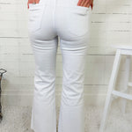 Person wearing white flared jeans and a pink sweater in a minimalistic setting.