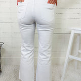 Person wearing white flared jeans and a pink sweater in a minimalistic setting.