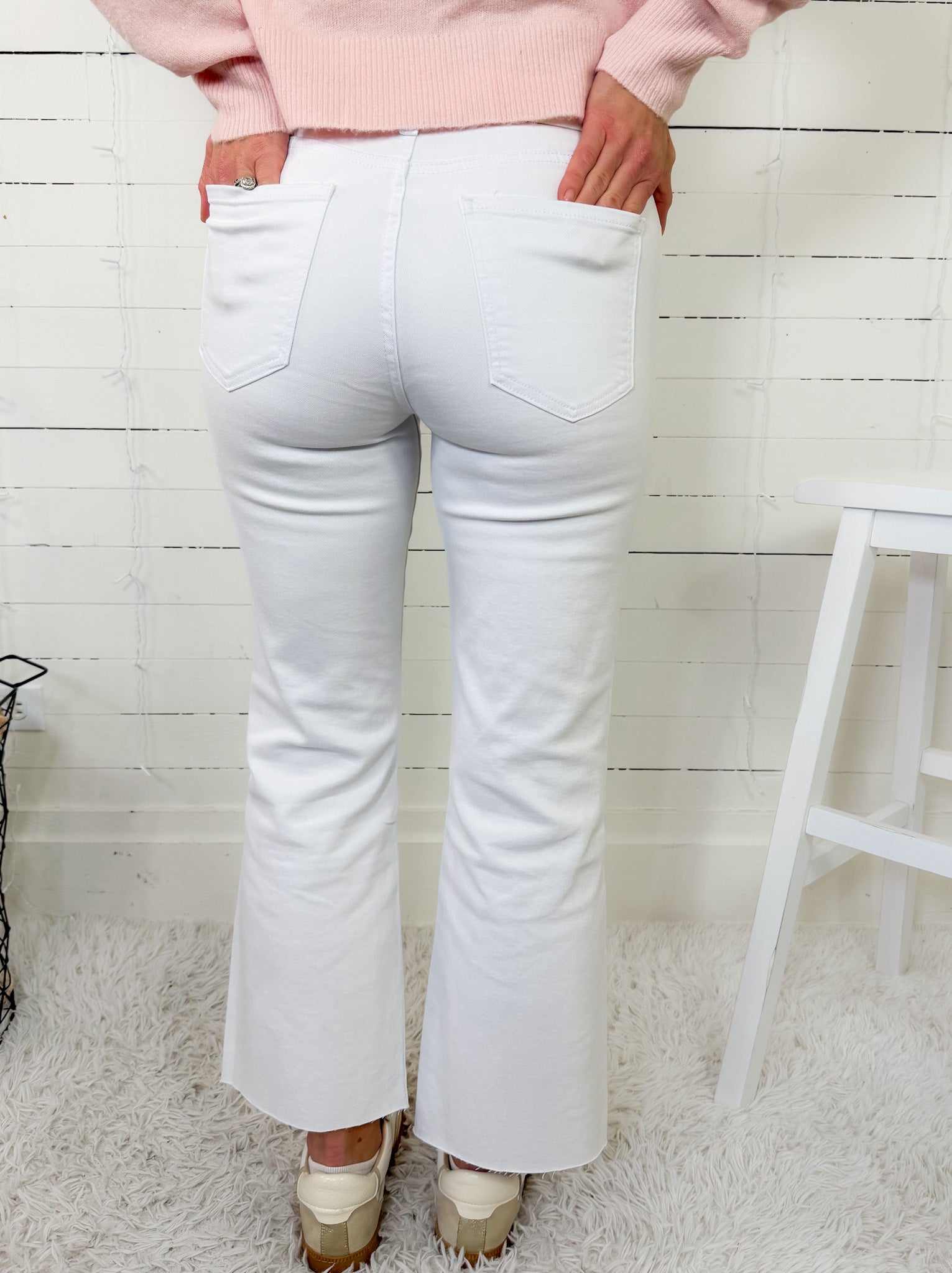 Person wearing white flared jeans and a pink sweater in a minimalistic setting.