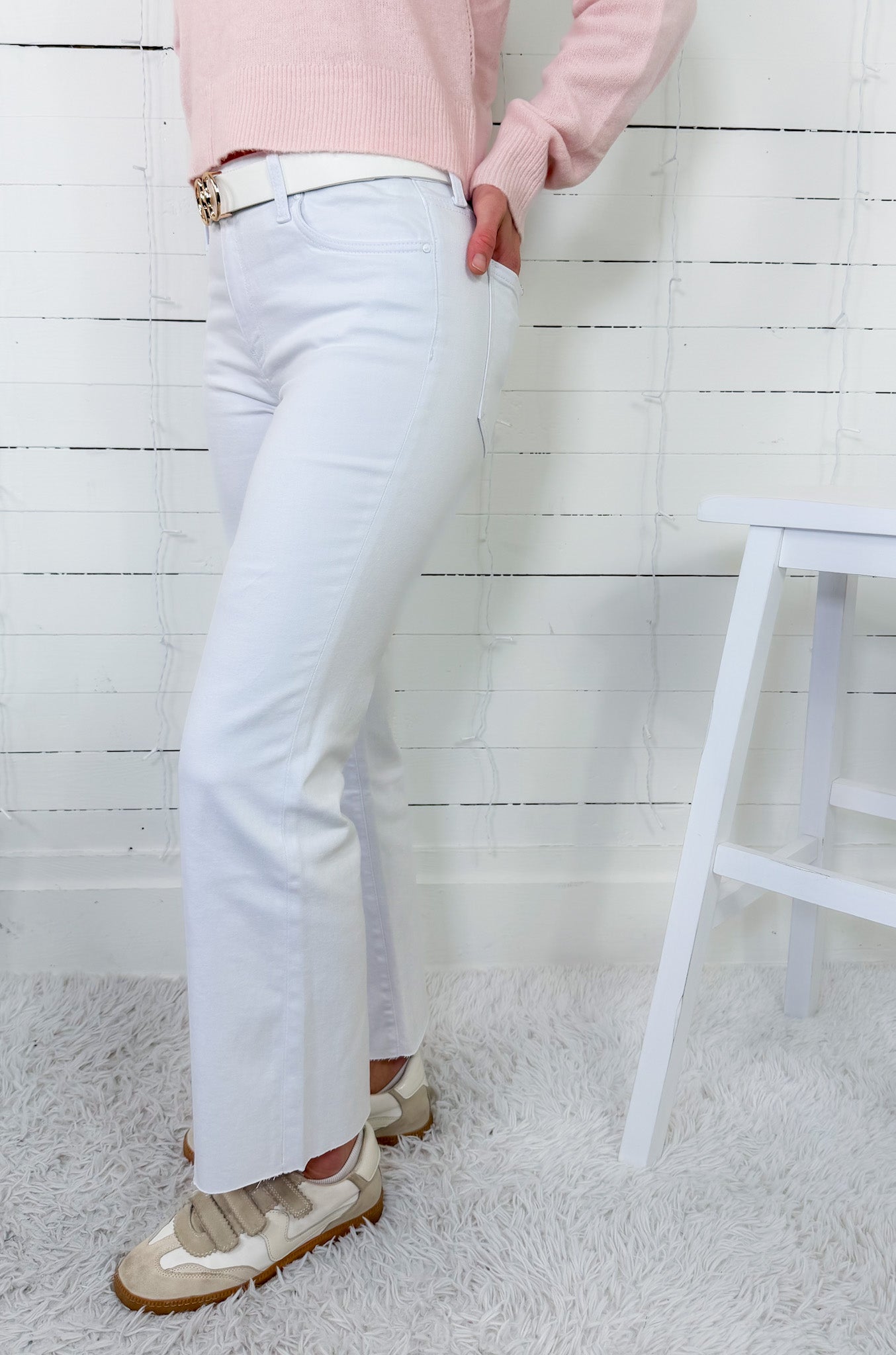 Person wearing light blue jeans and a pink sweater against a white wooden panel background.