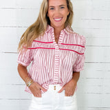Woman wearing a pink and white striped shirt with red accents against a white wooden panel background