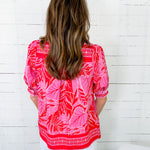 Person wearing a pink and red patterned top against a white wooden panel background