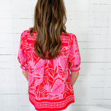 Person wearing a pink and red patterned top against a white wooden panel background