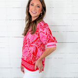 Woman wearing a pink and red patterned blouse against a white wooden background