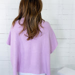 Person wearing a light purple sweater against a white wooden panel background