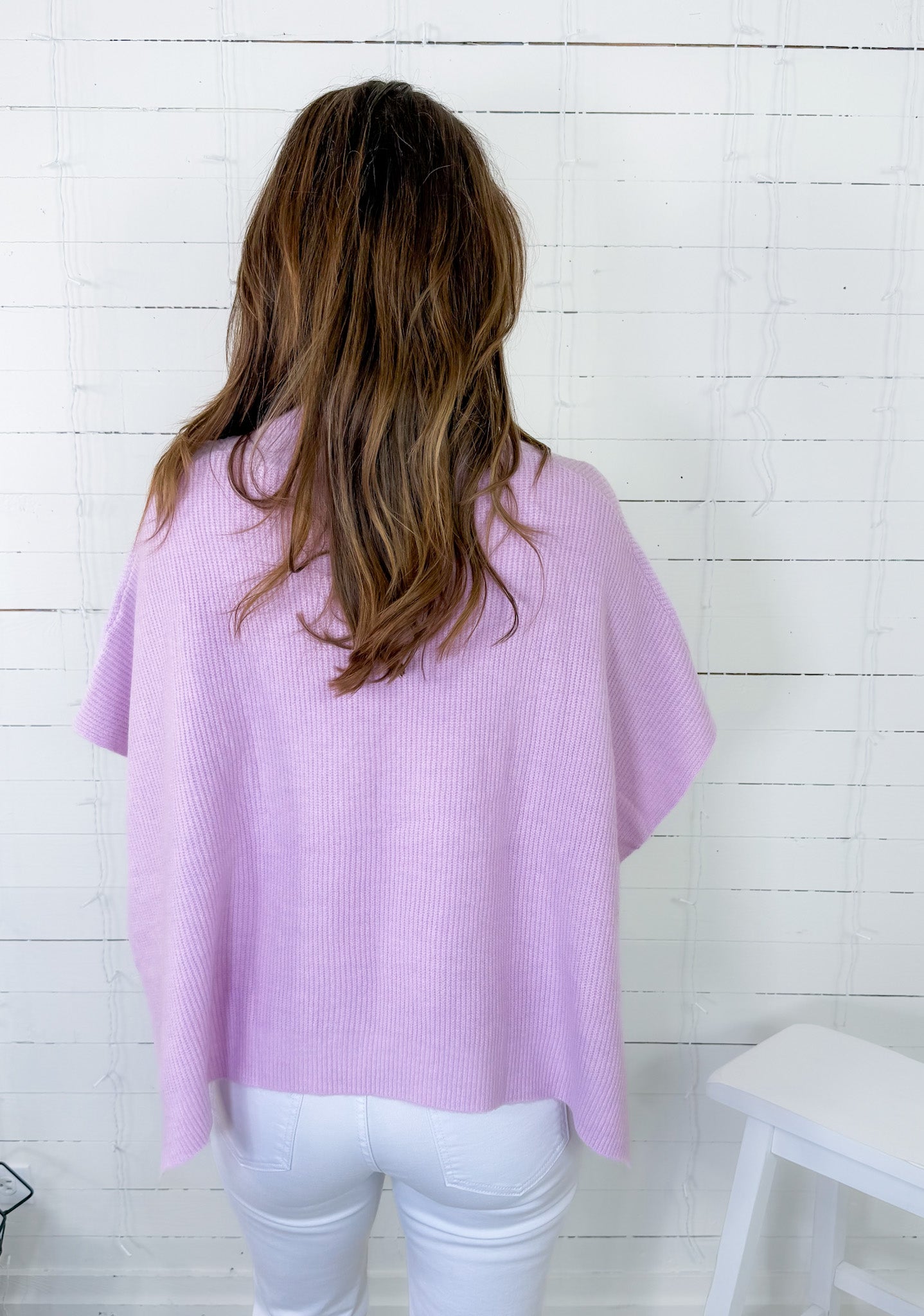Person wearing a light purple sweater against a white wooden panel background