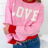 Person wearing a pink sweatshirt with 'LOVE' printed on it, red sleeves, and blue jeans.