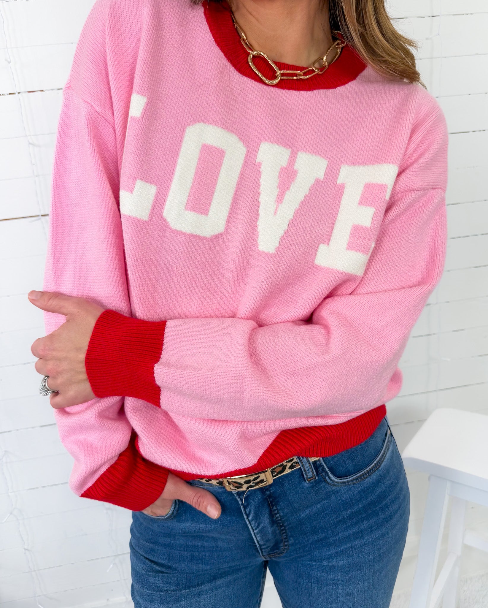 Person wearing a pink sweatshirt with 'LOVE' printed on it, red sleeves, and blue jeans.