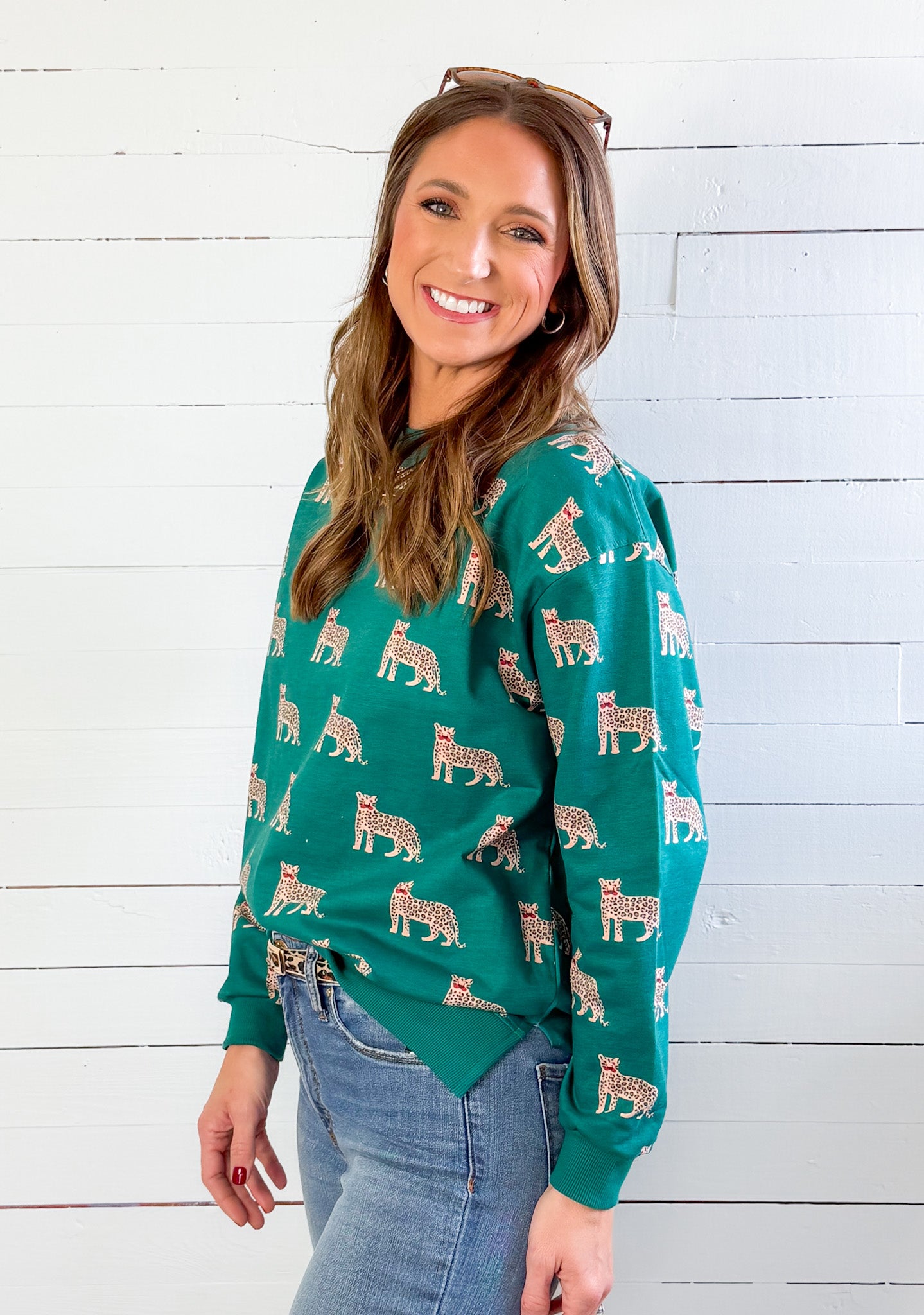 Woman wearing a green sweater with animal patterns against a white wooden wall.