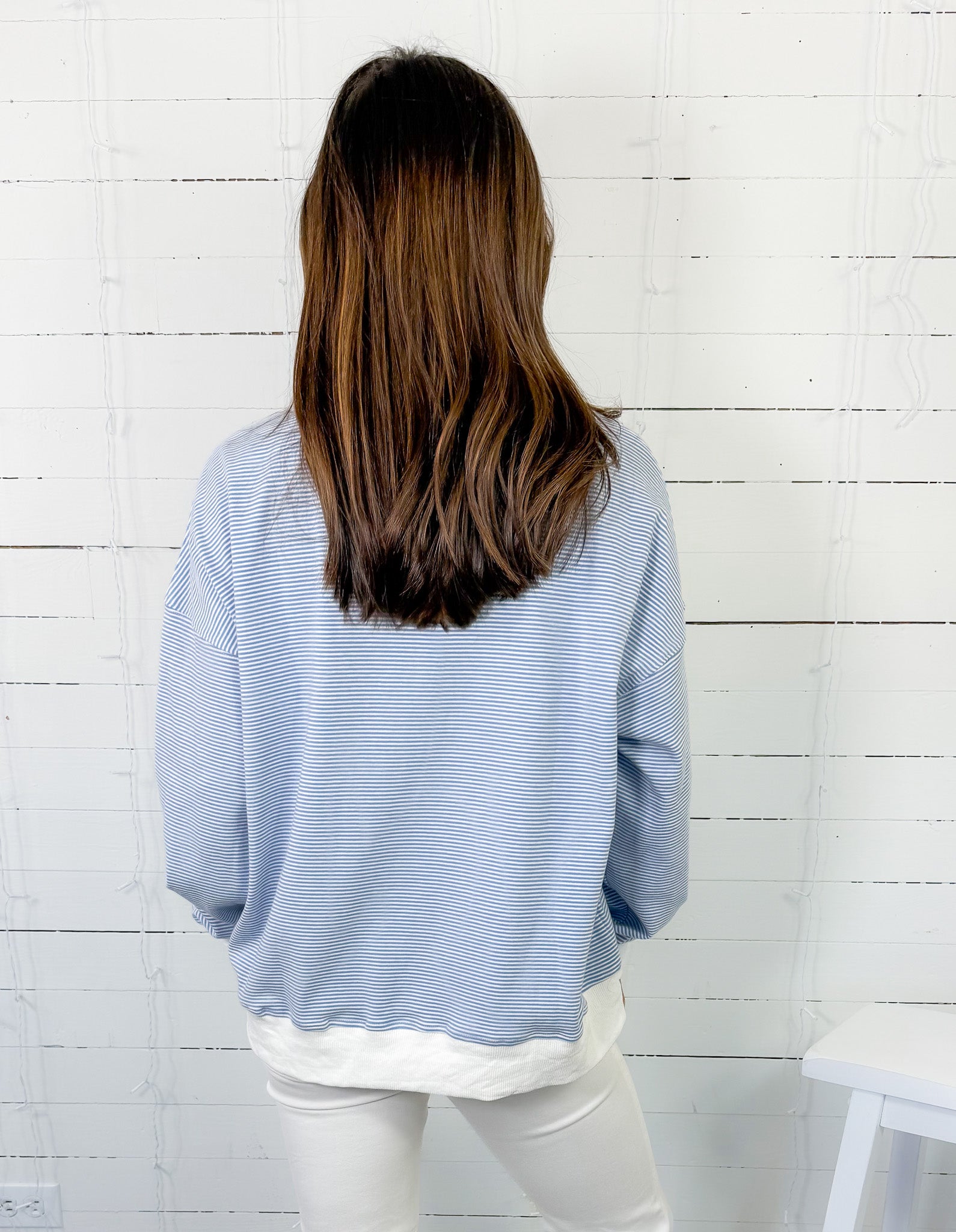 Person wearing a light blue sweater and white pants against a white wooden panel background