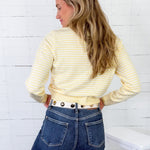 Woman wearing a yellow striped shirt and blue jeans against a white wooden panel background