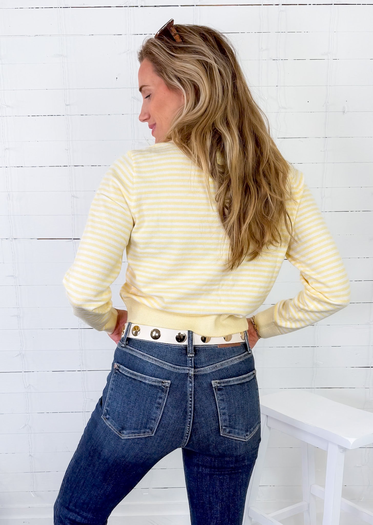 Woman wearing a yellow striped shirt and blue jeans against a white wooden panel background