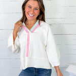 Woman wearing a white blouse with pink trim against a white brick wall.