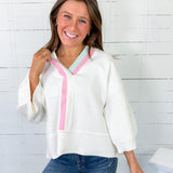 Woman wearing a white blouse with pink trim against a white brick wall.