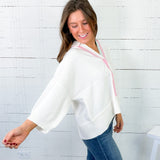 Woman wearing a white blouse with pink trim against a white brick wall.