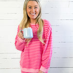 Woman wearing a pink and white striped outfit holding a mug against a white wooden background