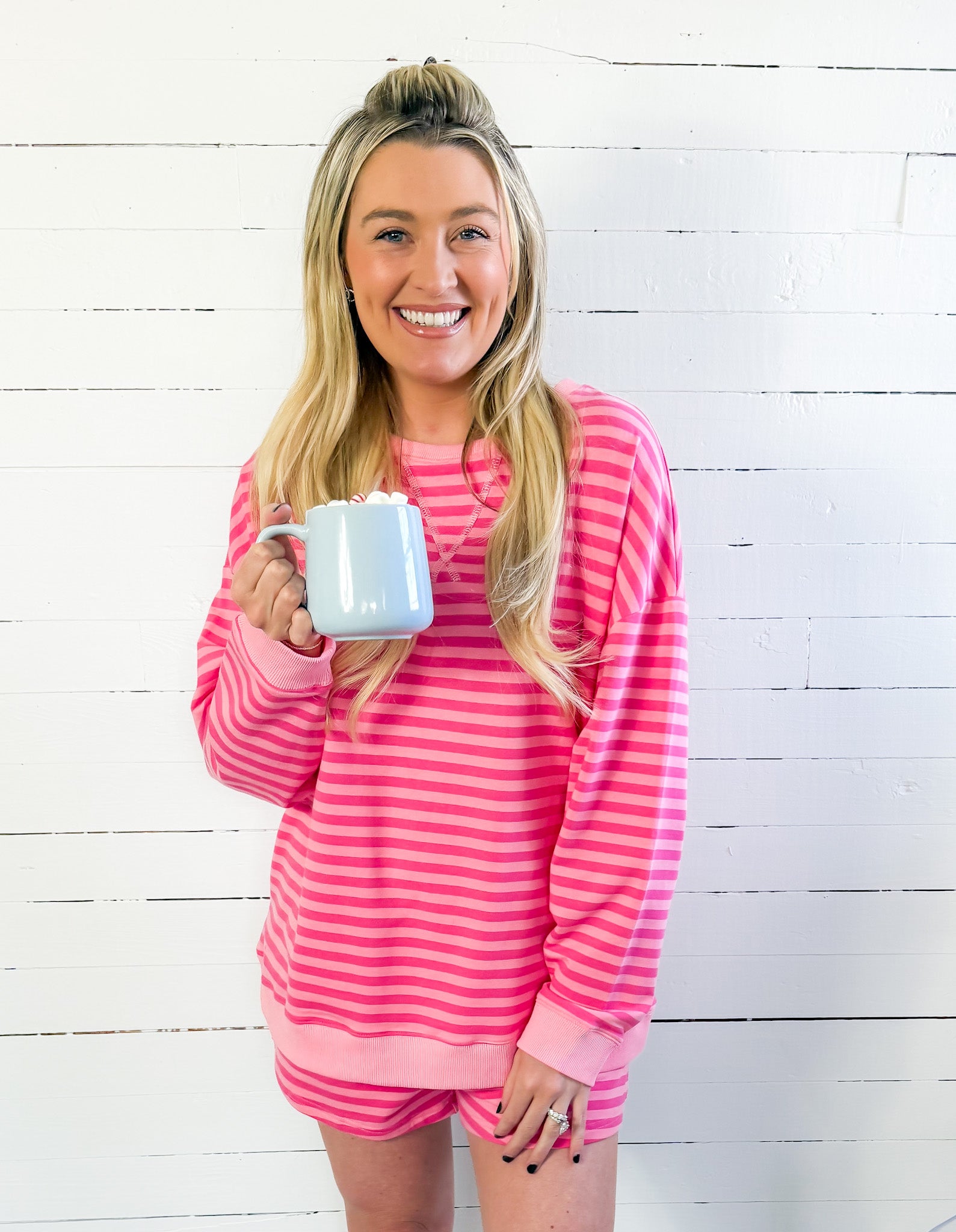 Woman wearing a pink and white striped outfit holding a mug against a white wooden background
