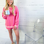 Woman in pink striped loungewear holding a mug, standing against a white wooden panel wall.