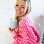 Woman in a pink and white striped shirt holding a small white container with a spoonful of hot chocolate.