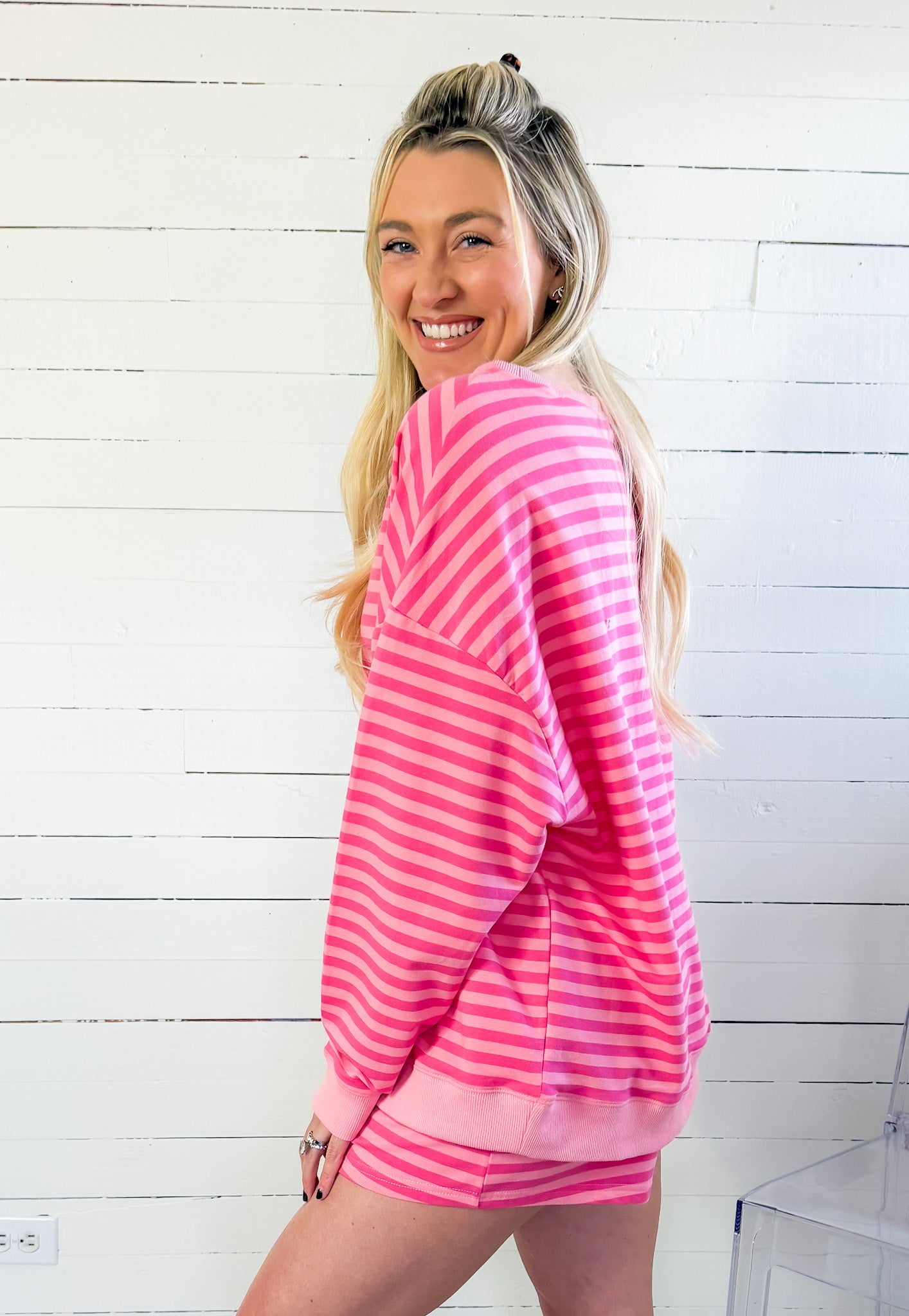 Woman wearing a pink and white striped outfit against a white wooden panel background