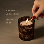 Candle being lit with text about burn time and ounces, on a neutral background.