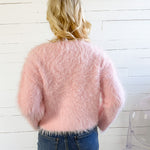 Person wearing a fluffy pink sweater and blue jeans against a white wooden panel background