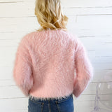 Person wearing a fluffy pink sweater and blue jeans against a white wooden panel background