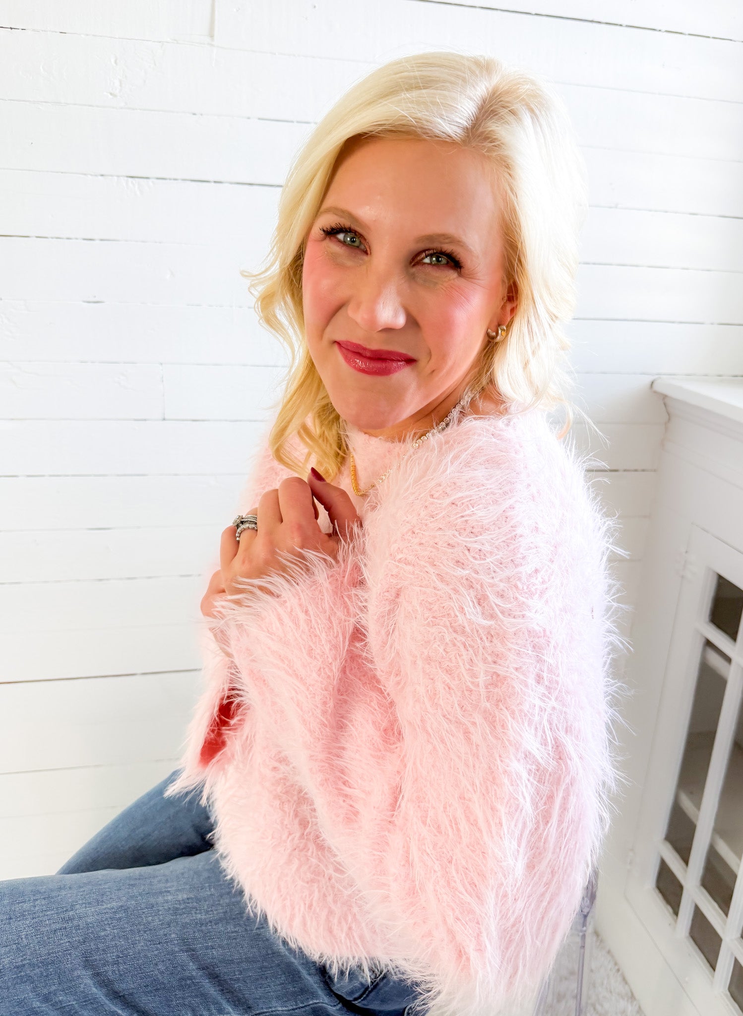 Woman wearing a pink fluffy jacket against a white wooden panel background