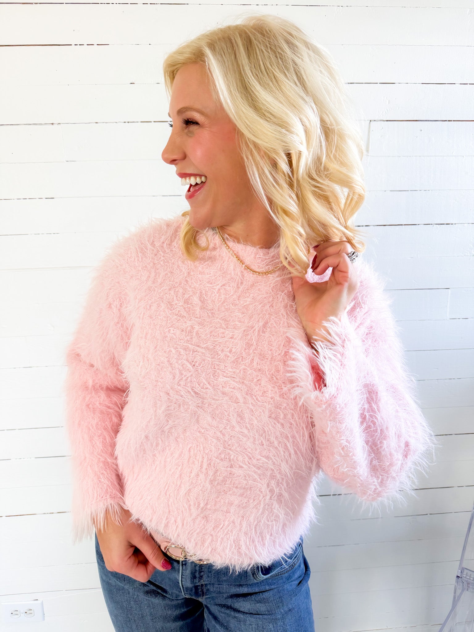 Woman wearing a pink fluffy sweater against a white wooden panel background