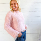 Woman wearing a pink fuzzy sweater and blue jeans against a white wooden panel background